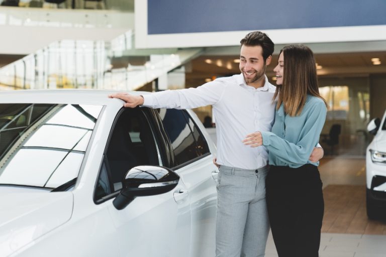 Un acheteur compare deux voitures, une neuve et une d’occasion, garées côte à côte sur le parking d’un concessionnaire