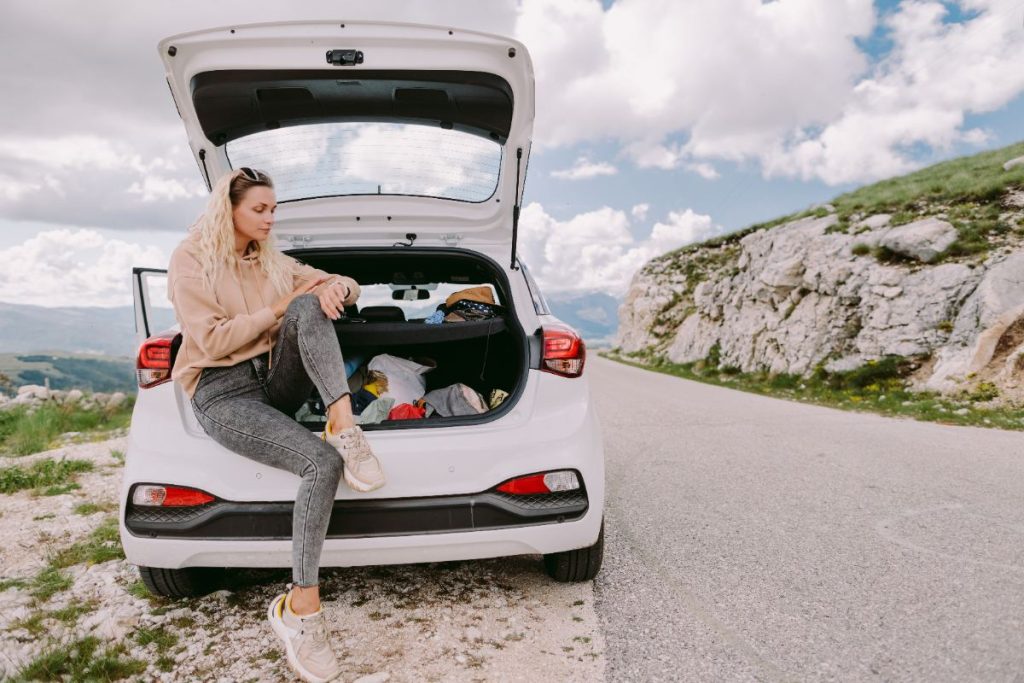 Une femme assise sur sa voiture au bord d'une auto-route
