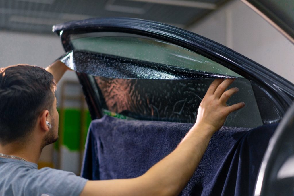 Un homme appliquant du film teinté sur la vitre de sa voiture