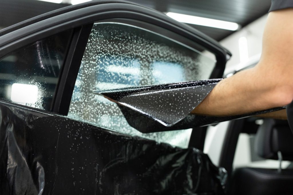 Main d'un homme qui met du film sur la vitre d'une voiture