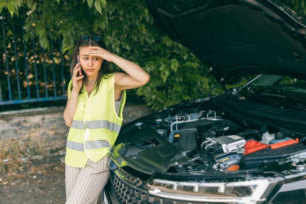 Une femme au téléphone devant sa voiture en panne