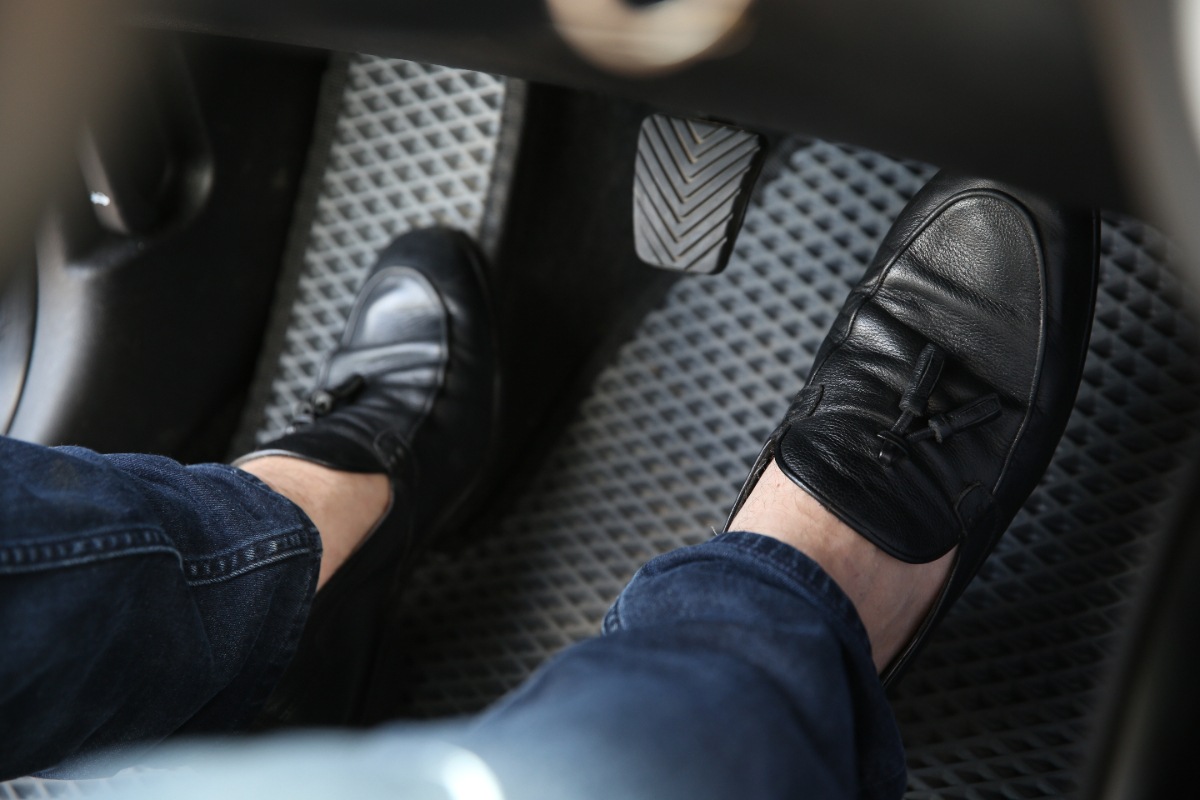 Une personne en jean et en mocassins appuyant sur l'embrayage de la voiture